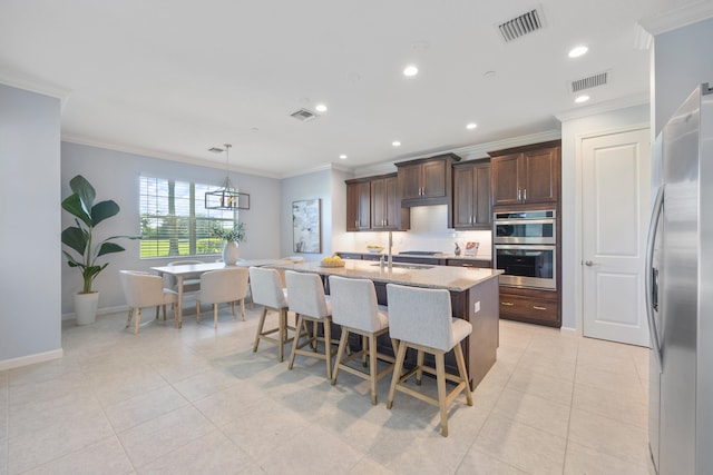 kitchen featuring hanging light fixtures, a kitchen bar, a center island with sink, appliances with stainless steel finishes, and ornamental molding