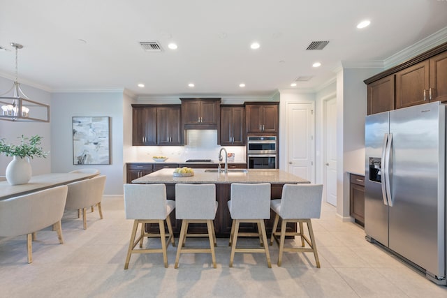 kitchen with ornamental molding, stainless steel appliances, sink, pendant lighting, and a center island with sink