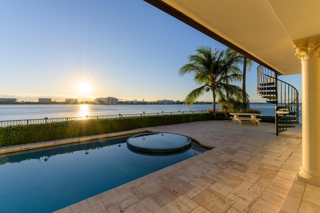 pool at dusk featuring a patio and a water view