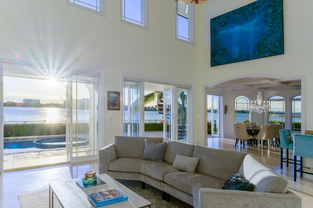 living room with a towering ceiling, a wealth of natural light, a notable chandelier, and a water view