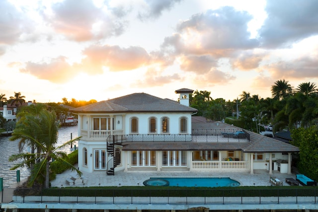 back house at dusk featuring a balcony, a water view, a fenced in pool, and a patio