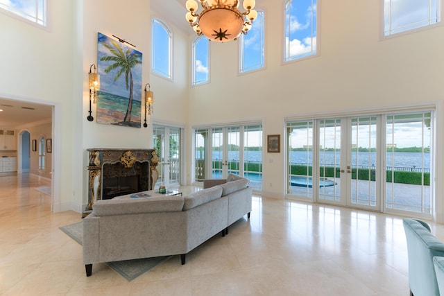 living room with a towering ceiling, a notable chandelier, french doors, and a water view