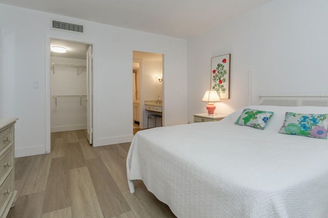 bedroom with a walk in closet, light wood-type flooring, a closet, and ensuite bath