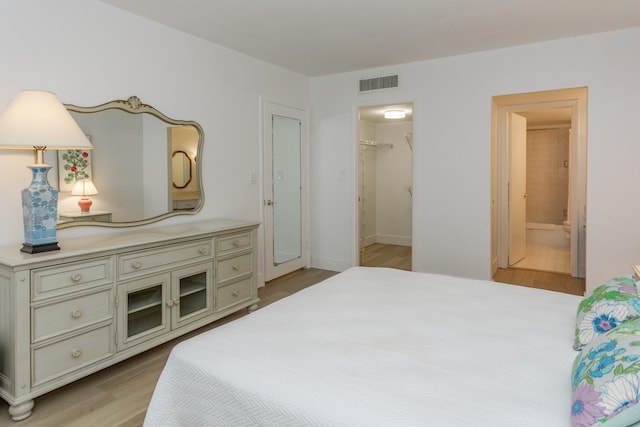 bedroom featuring a spacious closet, light wood-type flooring, ensuite bathroom, and a closet