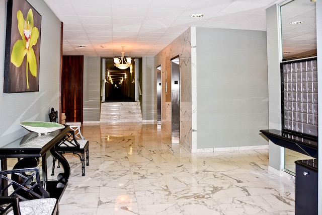 hall featuring a paneled ceiling, light tile patterned flooring, an inviting chandelier, and elevator