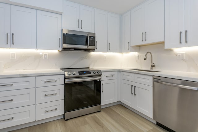 kitchen featuring backsplash, white cabinetry, light hardwood / wood-style floors, sink, and stainless steel appliances