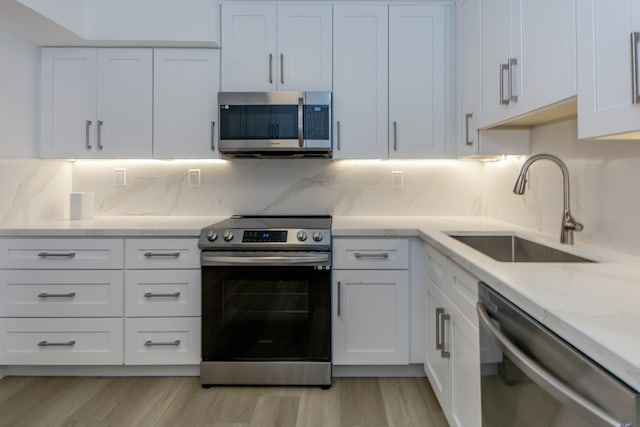 kitchen with appliances with stainless steel finishes, light hardwood / wood-style floors, decorative backsplash, white cabinetry, and sink