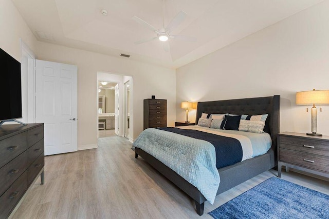 bedroom featuring connected bathroom, a tray ceiling, ceiling fan, and light hardwood / wood-style flooring