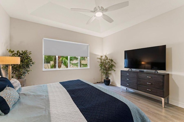 bedroom featuring a raised ceiling, light hardwood / wood-style floors, and ceiling fan