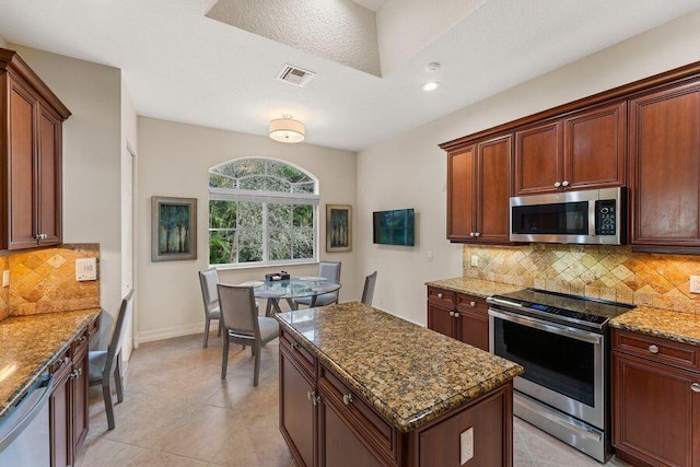 kitchen featuring a kitchen island, stainless steel appliances, light tile flooring, stone counters, and tasteful backsplash