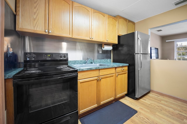 kitchen with black electric range oven, light hardwood / wood-style floors, stainless steel refrigerator, and sink