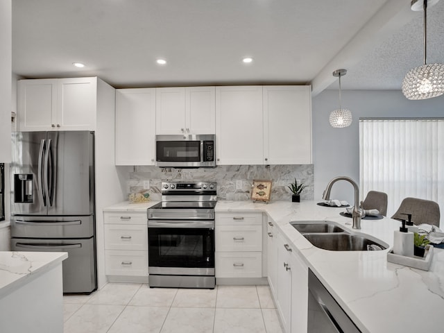 kitchen with stainless steel appliances, decorative light fixtures, light stone countertops, white cabinetry, and sink