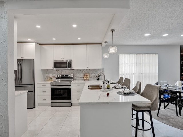 kitchen with sink, light tile floors, hanging light fixtures, white cabinets, and appliances with stainless steel finishes