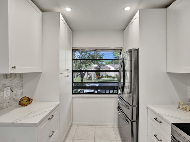 kitchen featuring stainless steel refrigerator, white cabinetry, and light stone counters