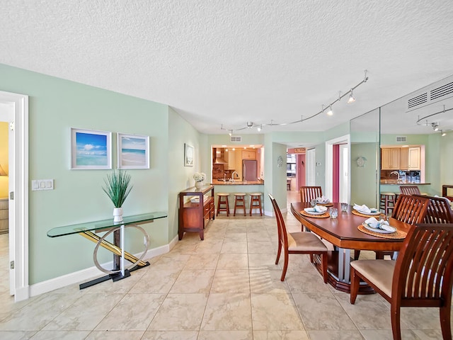 dining area featuring a textured ceiling, rail lighting, and light tile flooring