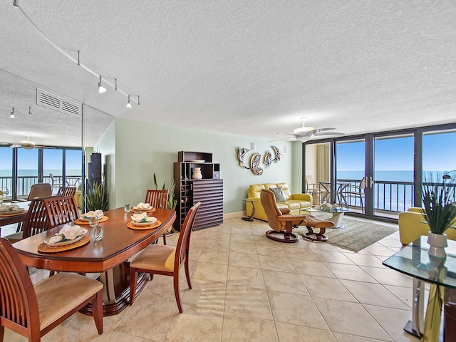 dining space featuring light tile flooring, ceiling fan, rail lighting, a textured ceiling, and a water view