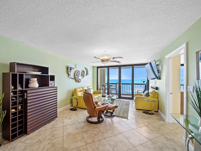 tiled living room featuring a water view, ceiling fan, a textured ceiling, and a wall of windows