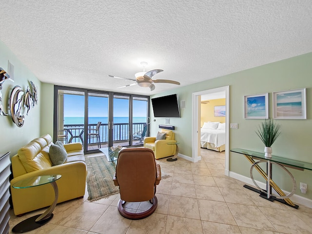 tiled living room with a water view, a textured ceiling, expansive windows, and ceiling fan