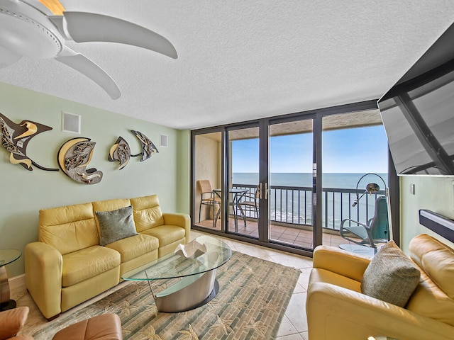 living room featuring a water view, a textured ceiling, light tile flooring, and ceiling fan