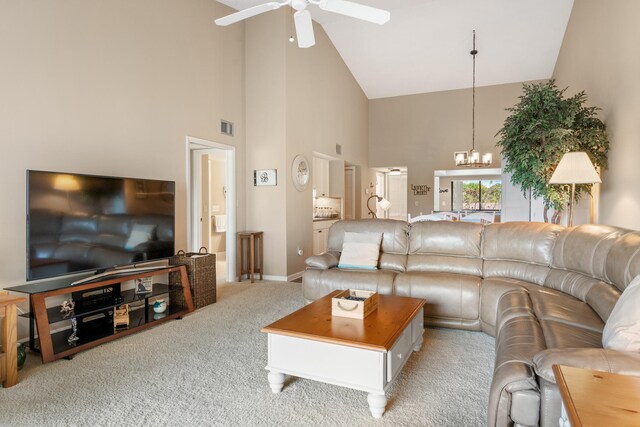 carpeted living room with high vaulted ceiling and ceiling fan with notable chandelier