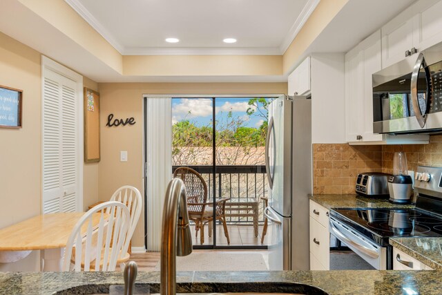 kitchen featuring white cabinetry, stainless steel appliances, dark stone counters, tasteful backsplash, and crown molding