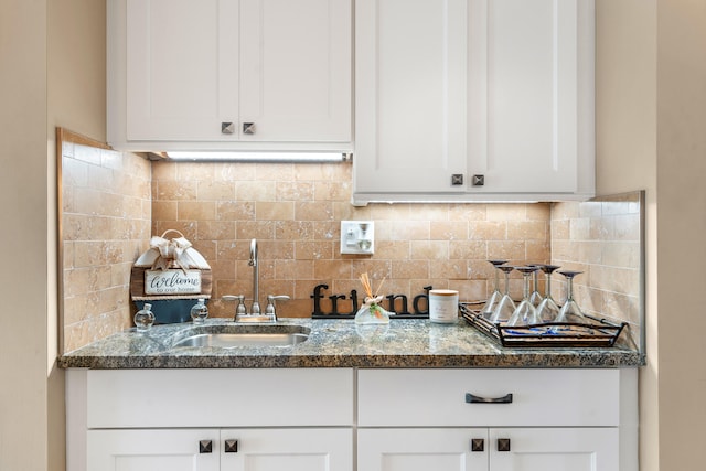 interior space with backsplash, dark stone countertops, white cabinetry, and sink