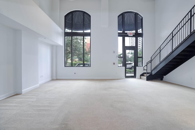 foyer entrance featuring a towering ceiling, a healthy amount of sunlight, and light colored carpet