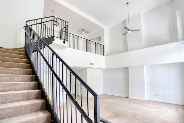 stairway featuring light carpet, ceiling fan, and a high ceiling