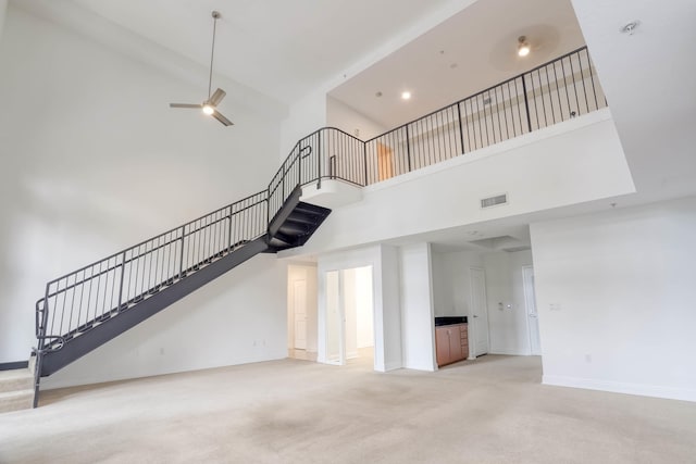 unfurnished living room with light carpet, ceiling fan, and a towering ceiling