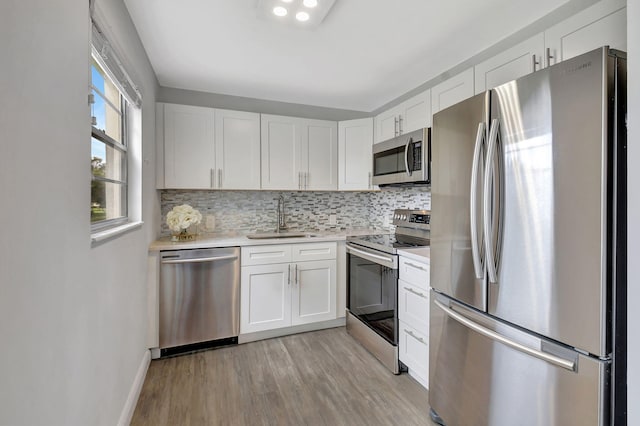 kitchen featuring tasteful backsplash, appliances with stainless steel finishes, white cabinetry, light wood-type flooring, and sink