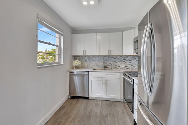 kitchen with appliances with stainless steel finishes, sink, white cabinets, decorative backsplash, and light hardwood / wood-style flooring