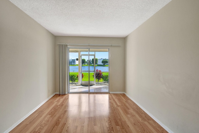 unfurnished room featuring a water view, a textured ceiling, and light wood-type flooring