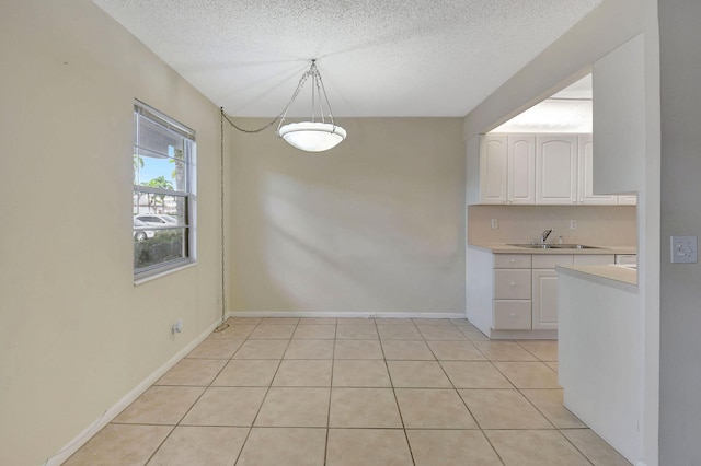 unfurnished dining area featuring sink, a textured ceiling, and light tile patterned floors