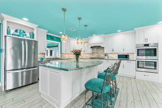 kitchen with a kitchen island, white cabinets, appliances with stainless steel finishes, tasteful backsplash, and decorative light fixtures