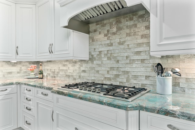 kitchen with light stone countertops, white cabinetry, backsplash, and premium range hood