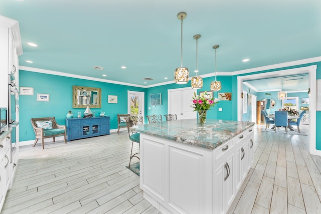 kitchen with hanging light fixtures, ornamental molding, white cabinets, light hardwood / wood-style flooring, and a center island