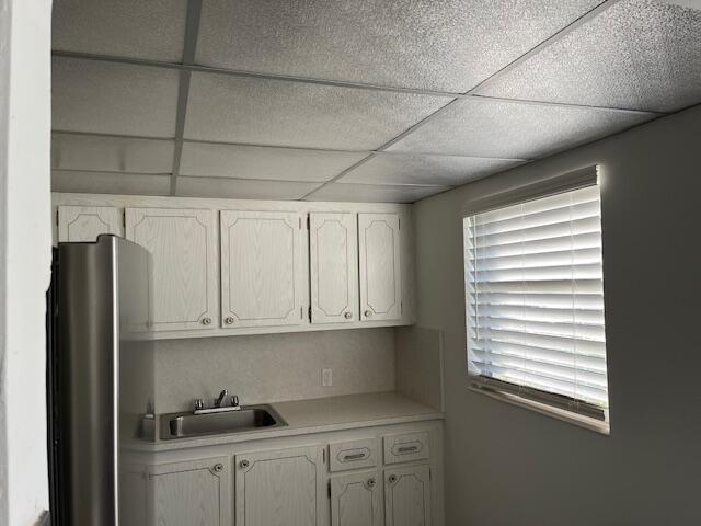 kitchen with sink, a healthy amount of sunlight, white cabinets, and a paneled ceiling