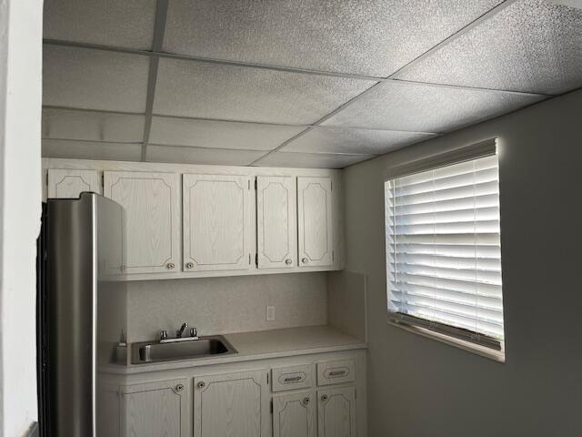 kitchen with sink, white cabinetry, stainless steel fridge, and a drop ceiling