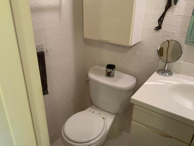 bathroom with toilet, vanity, and tile walls