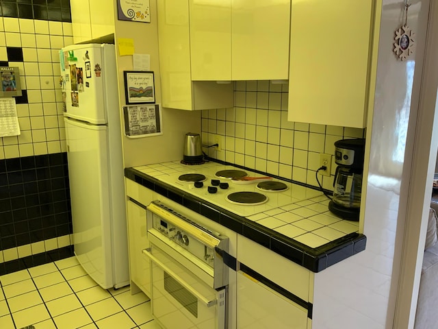 kitchen featuring tile counters, white appliances, tasteful backsplash, and light tile floors