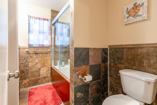 bathroom featuring shower / bath combination with glass door, toilet, and tile walls