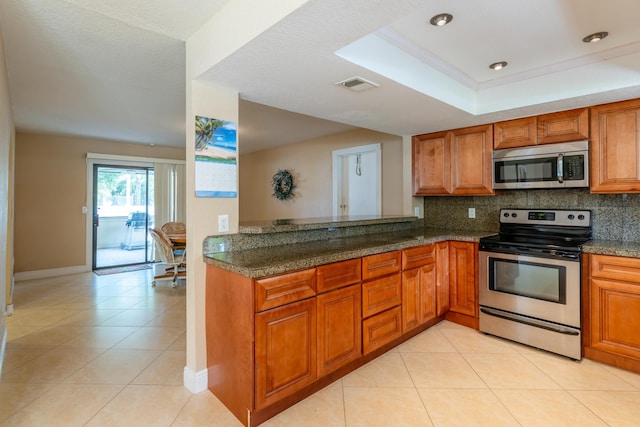 kitchen with stainless steel appliances, decorative backsplash, dark stone counters, and a tray ceiling