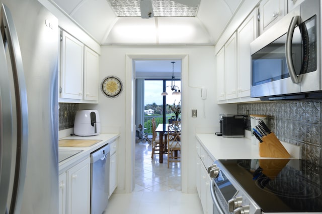 kitchen with white cabinetry, backsplash, appliances with stainless steel finishes, light tile floors, and a chandelier