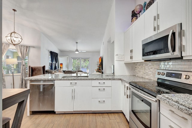 kitchen featuring light wood-type flooring, pendant lighting, white cabinets, and stainless steel appliances