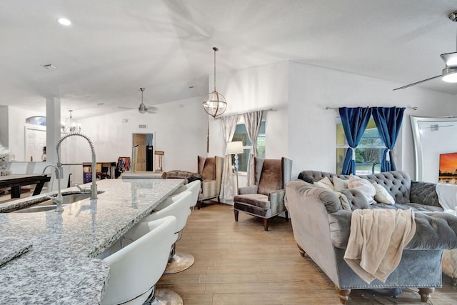 living room featuring ceiling fan with notable chandelier, sink, light wood-type flooring, and lofted ceiling