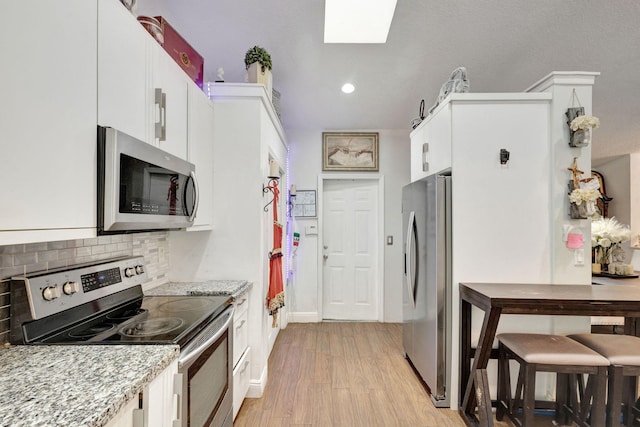 kitchen featuring white cabinets, appliances with stainless steel finishes, light stone counters, and light hardwood / wood-style flooring