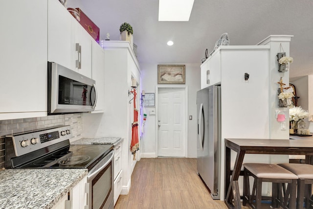 17891 N 86th St N, The Acreage, FL 33470 - kitchen featuring appliances with stainless steel finishes, light wood-style flooring, a skylight, white cabinets, and tasteful backsplash