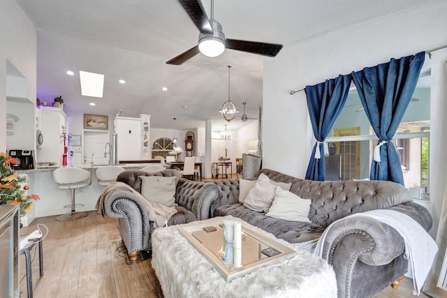 living room featuring ceiling fan with notable chandelier, light wood-type flooring, and a skylight