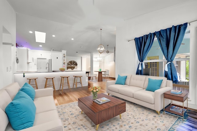 living room featuring light hardwood / wood-style flooring, a skylight, and an inviting chandelier