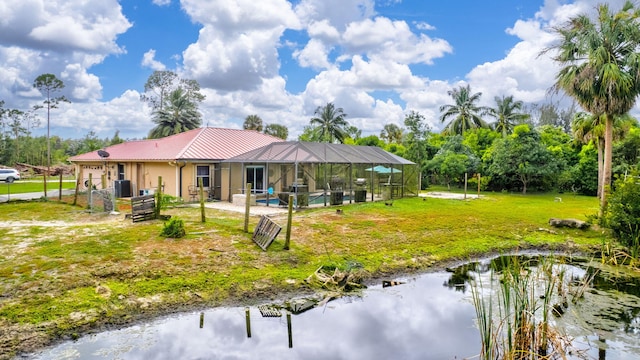 rear view of property featuring a lanai, a water view, a lawn, and a patio area